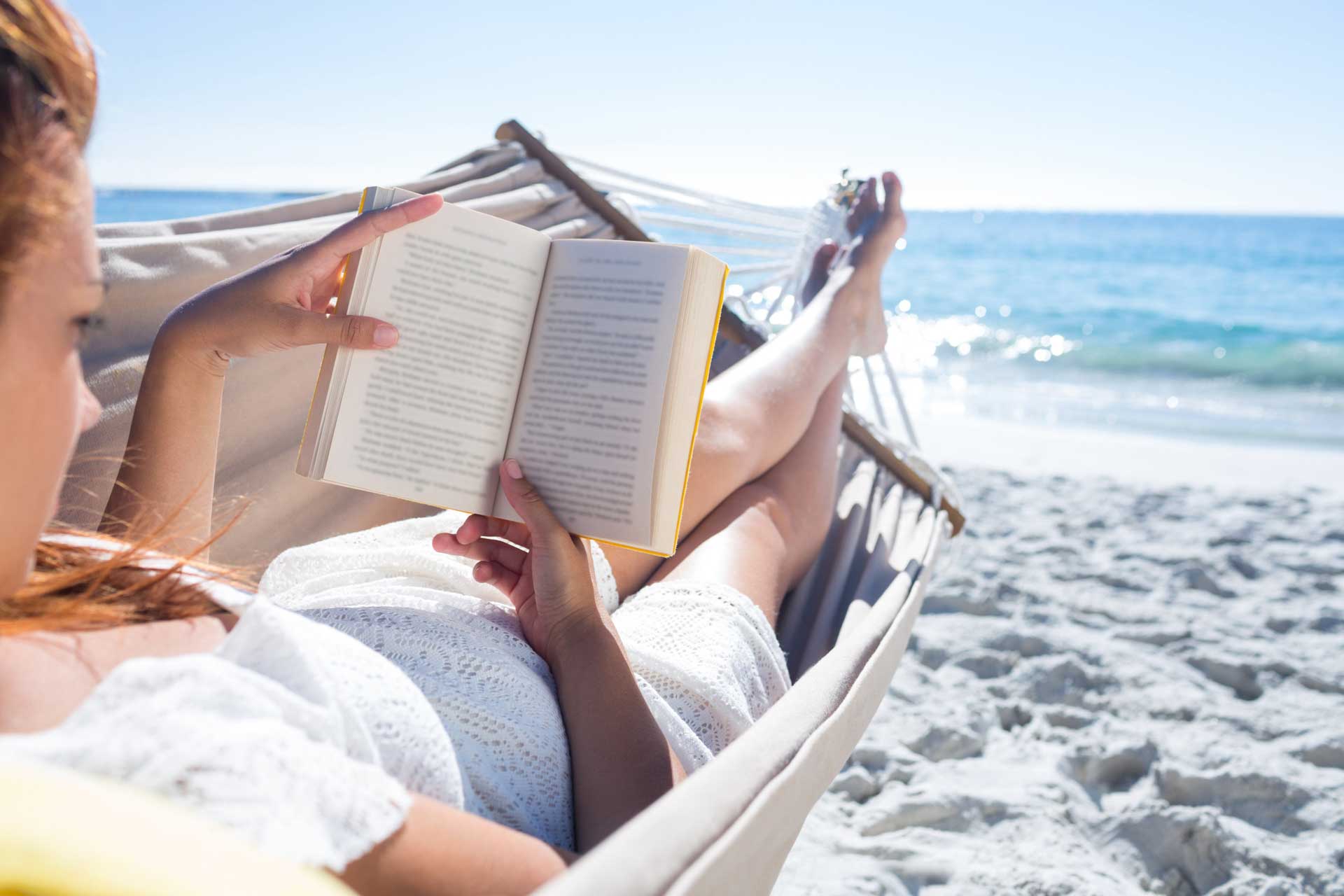 Brunette reading a book while relaxing in the hammock at the beach